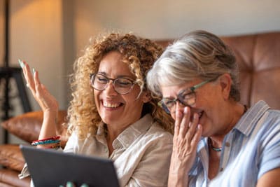 senior and adult daughter laughing and looking at a tablet together