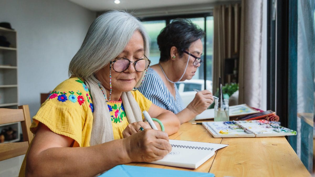 senior woman friends enjoying drawing with pen while setting in living room at home, Hobby and relaxing concept