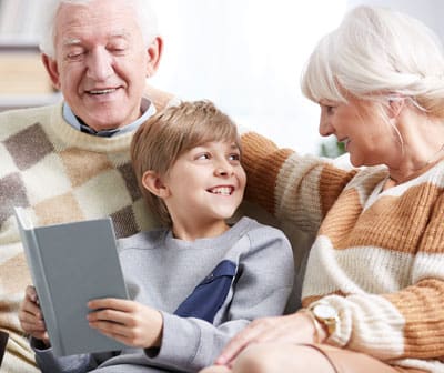 senior grandparents sitting with young grandson reading a book