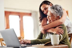 woman hugging her grandmother before helping her with her finances on a laptop