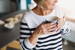 Senior woman holding a cup of coffee in the kitchen.