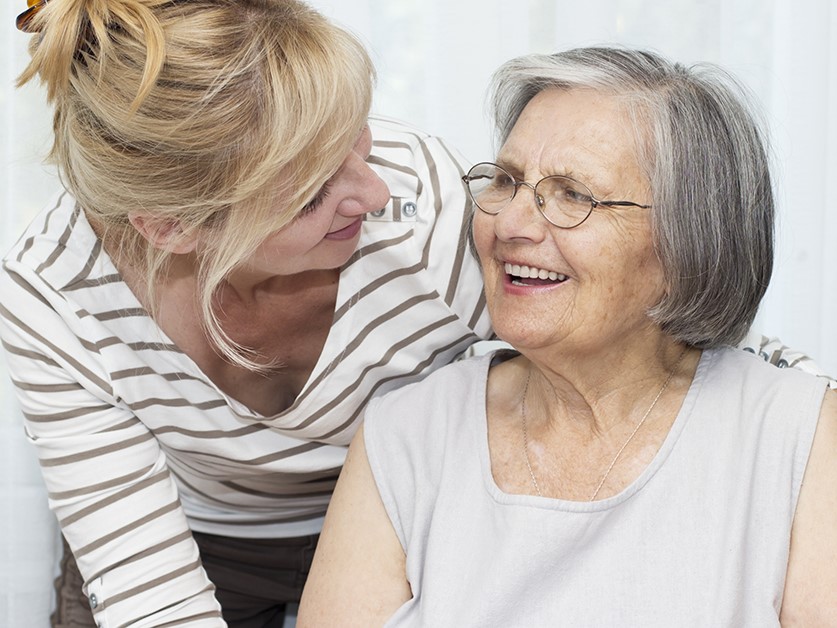 adult daughter leaning down to smile at her senior mother