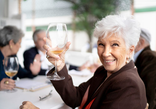 senior woman smiling while raising a glass of white wine