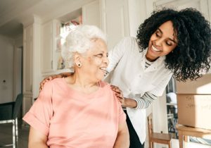 Home caregiver smiling and resting her hands on senior woman