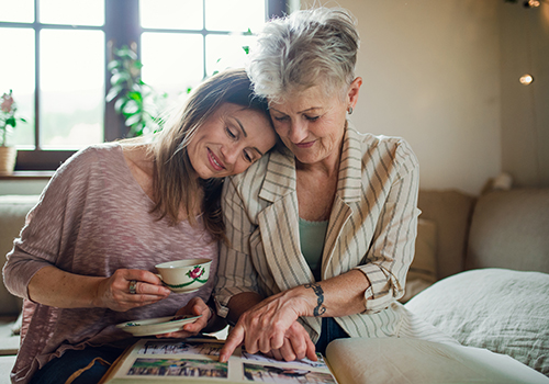 A senior mother with adult daughter indoors at home, looking at family photographs.