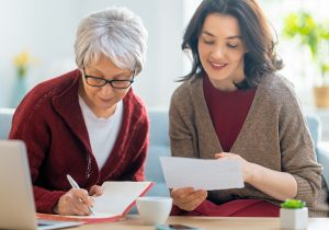 Two women, sitting on the sofa with a paper receipt, are calculating expenses, managing the family budget.