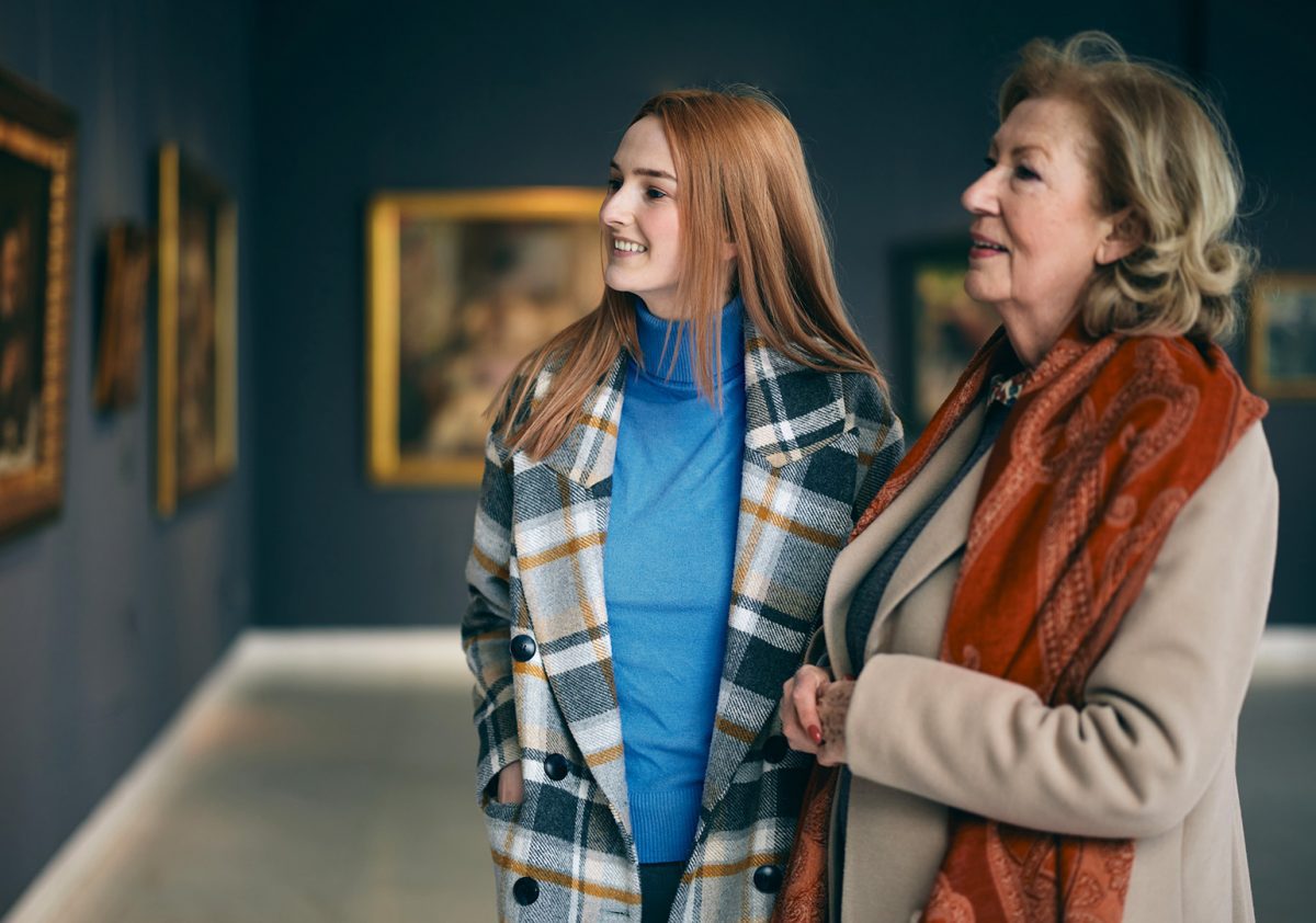 Grandmother and adolescent granddaughter are looking at the paintings in the art gallery.