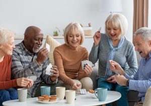 Happy senior friends playing cards while chilling together at home