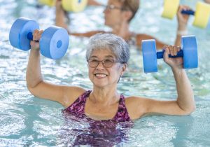 A group of happy seniors taking a water aerobics class at a community centre.