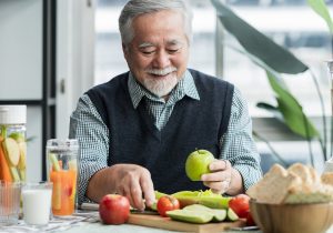 Asian elder senior male vlog teach cooking on mobile phone. Male old man vlogs, Old chef records a video tutorial on his phone about preparing heathy salad and infused water at home