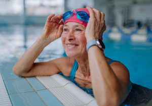 A happy senior woman in swimming pool, leaning on edge