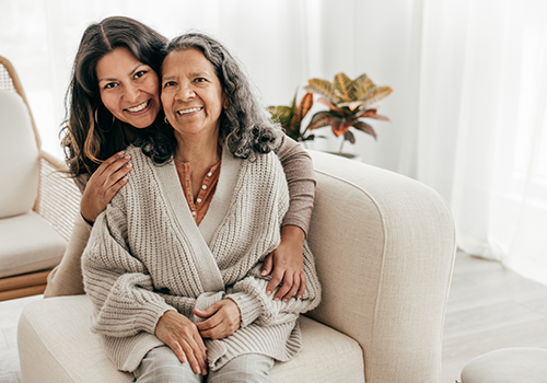 adult daughter hugging her senior mother while they're both smiling