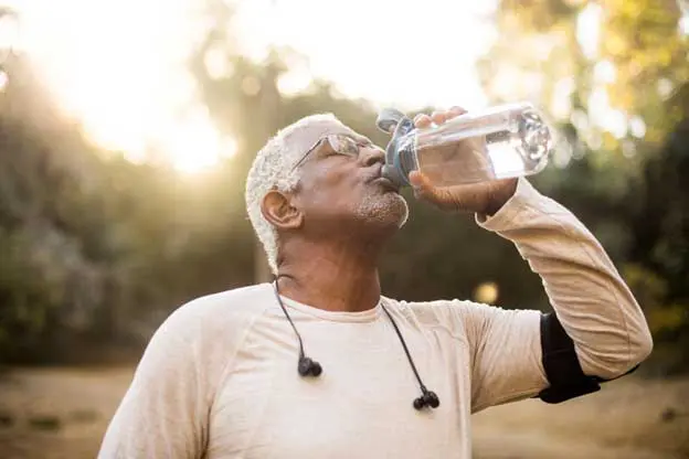 senior man drinking water on a run outside