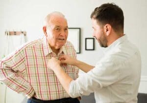 adult son helping button his senior father's shirt