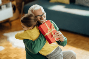 senior man holding a wrapped gift and hugging his granddaughter