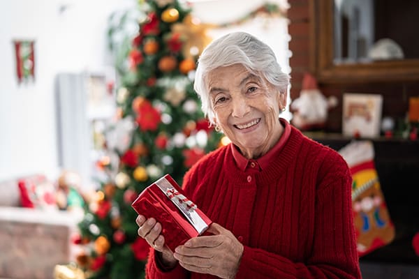 Senior woman at home holding a christmas present while looking at camera smiling with a smile