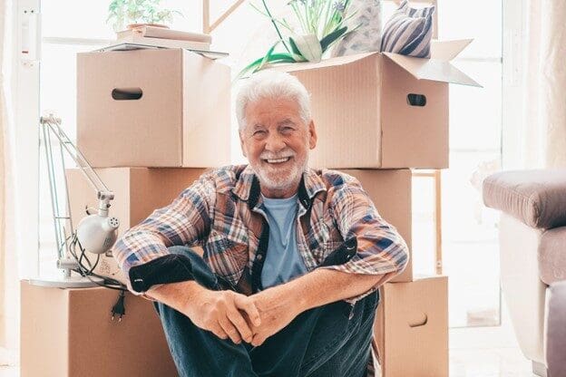 smiling senior man sitting in front of packed moving boxes