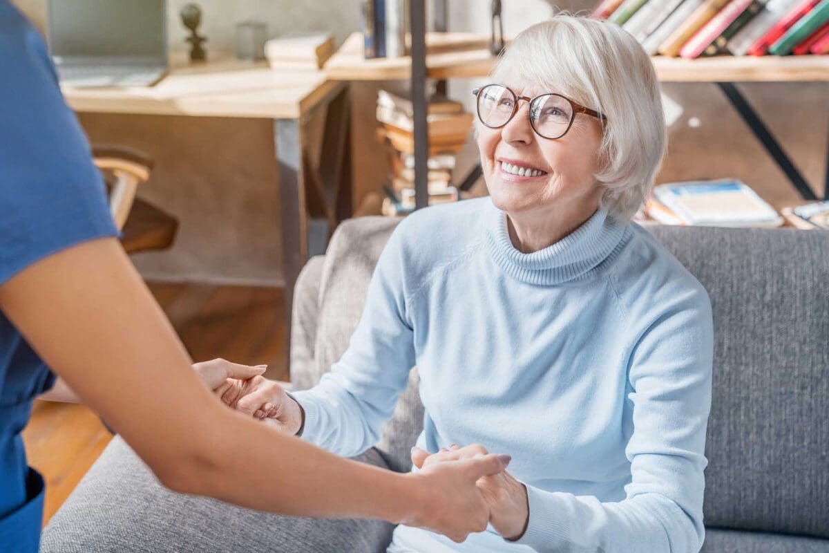 caregiver helping a senior woman stand up from the couch