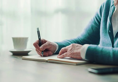 Senior woman sitting at desk and writing down notes on a notebook